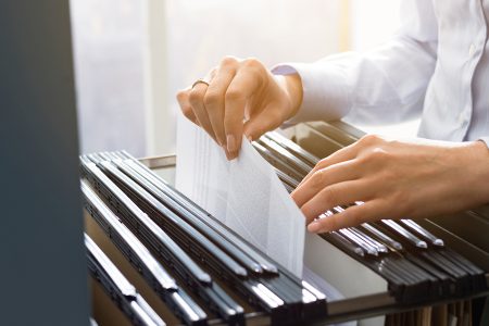 Professional female office clerk searching files and paperwork in the filing cabinet