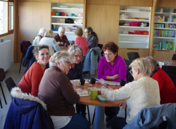 Un groupe d'adultes est en train de jouer à des jeux de société. Ils sont une quinzaine et répartis sur deux tables.