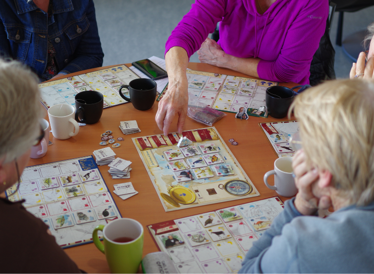 Partie de jeu de société en cours sur une table de la ludothèque. On voit des mains qui manipulent les pièces de jeux