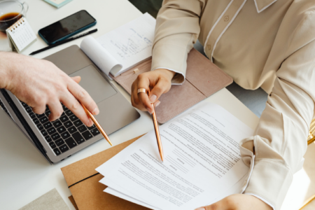 Personne qui travaille, sur son bureau il y a un ordinateur et un dossier sur lequel elle est en train d'écrire